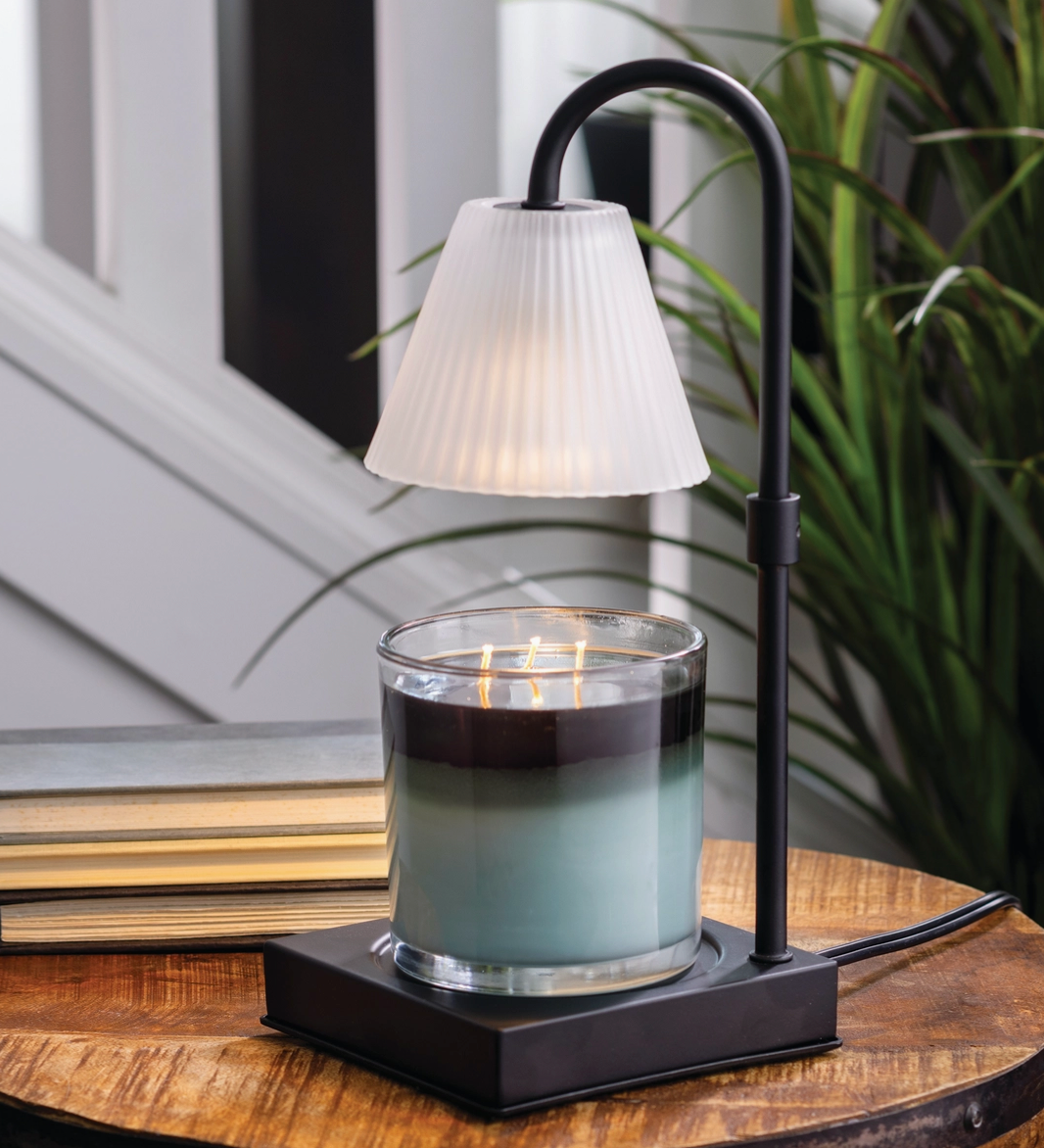 Candle in a glass holder with a black metal stand on a wooden surface, with a blurred background.