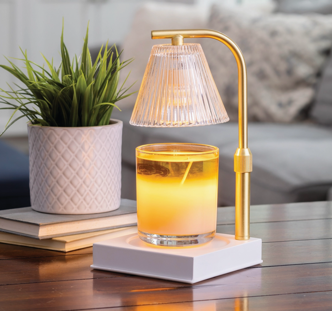 Gold table lamp with a glass candle holder on a wooden surface next to a potted plant.
